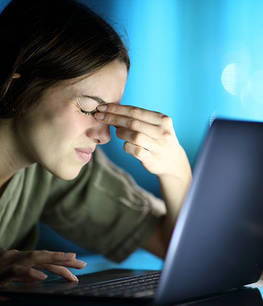 A person rubbing their eyes at a laptop